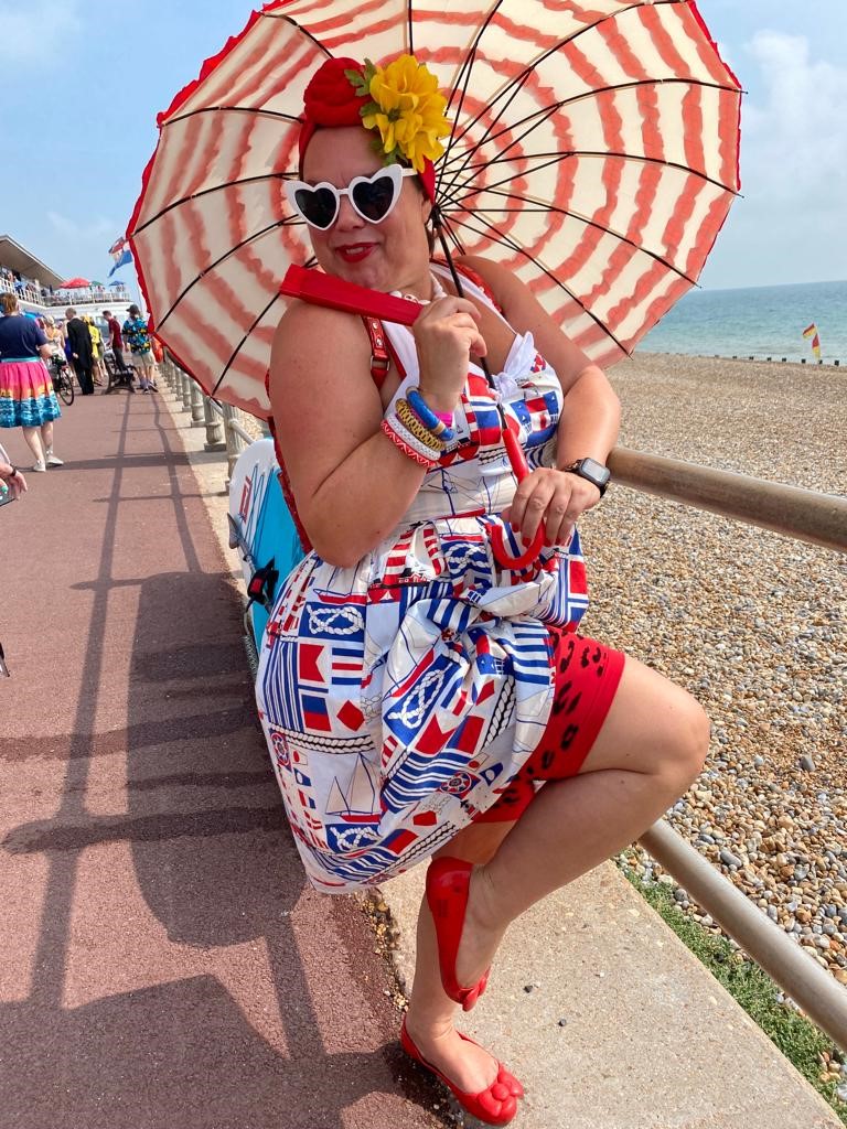 A lovely lady dressed up in red, white and blue with a parasol next to the beach