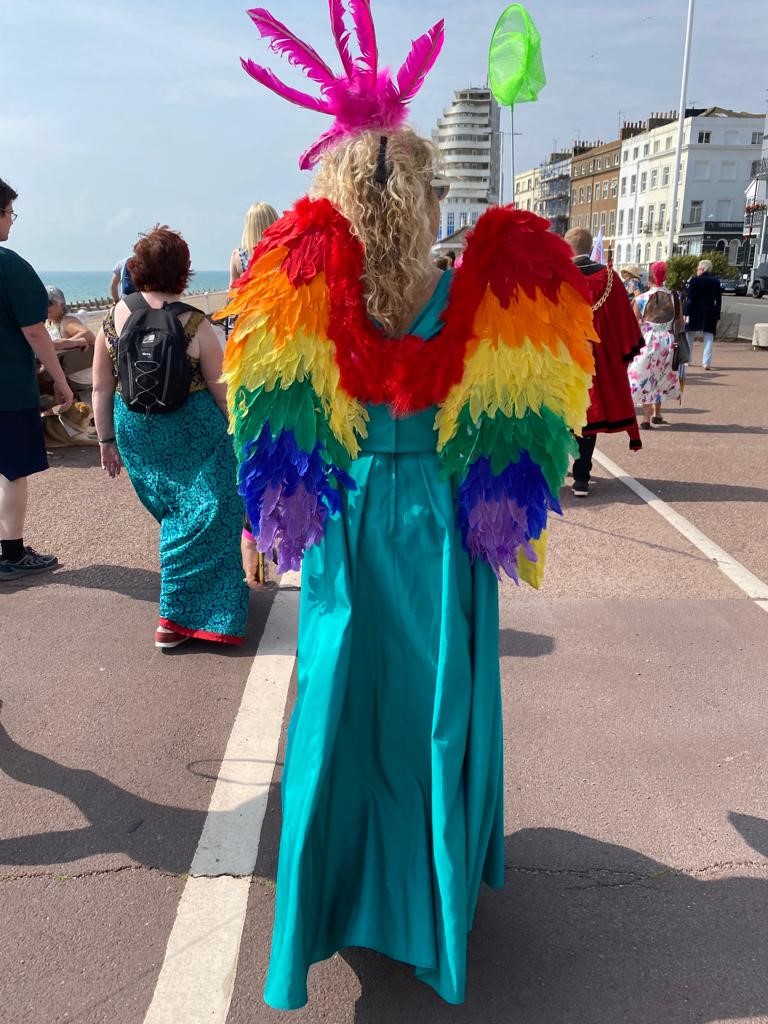 A lady walking along the promenade at St Leonards wearing a long dress and rainbow wings