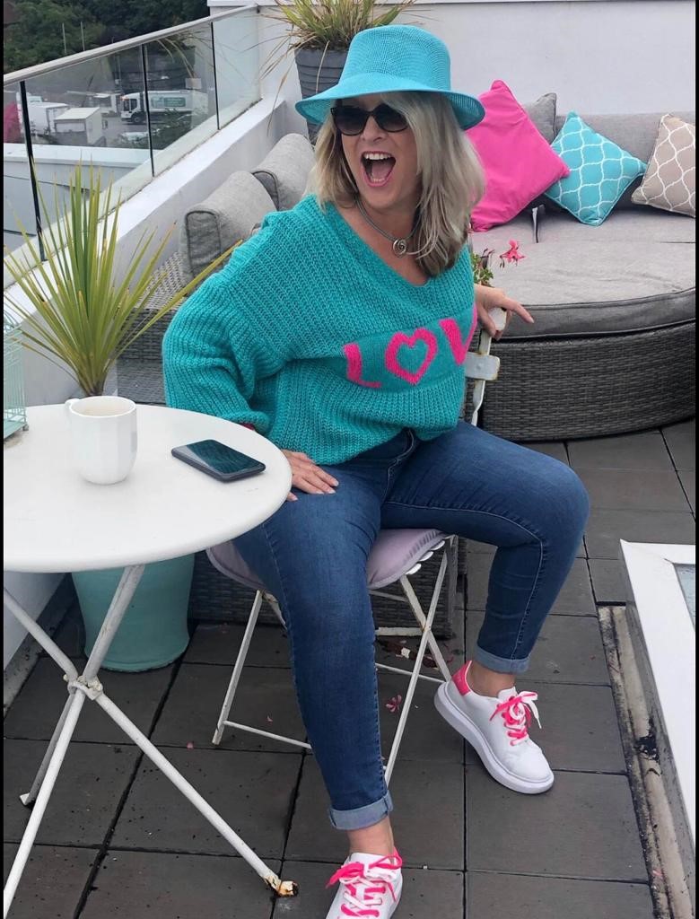 Sarah wearing jeans, a LOVE jumper and hat in turquoise