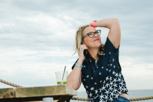 Sarah by the sea with her hand in her hair looking upwards in thought - thinking about life