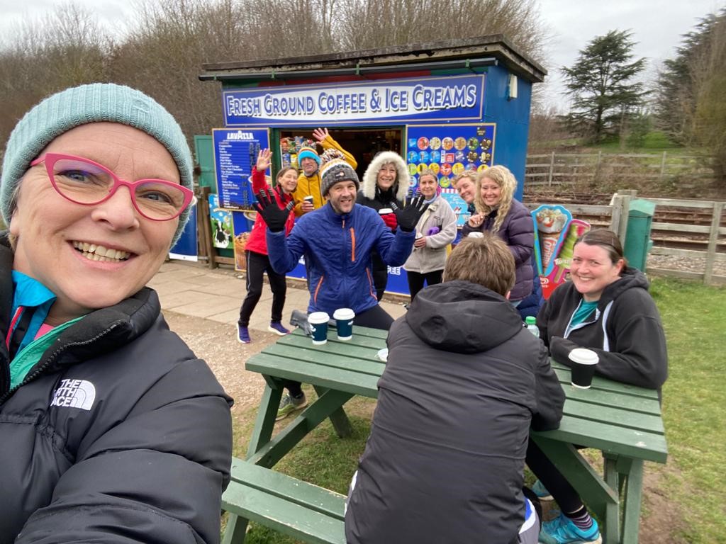 Sarah and Gareth with friends by picnic tables and a coffee & ice-cream kiosk, post parkrun