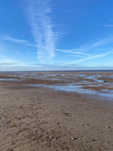 Blue skies, vapor trails, sea and sand on an open beach in Norfolk in January.